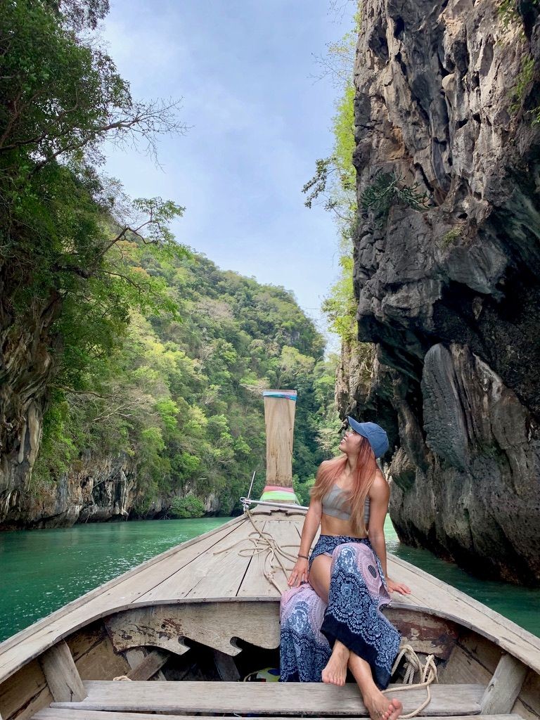 Woman sitting on a boat in a narrow canyon with green water and rocky cliffs.